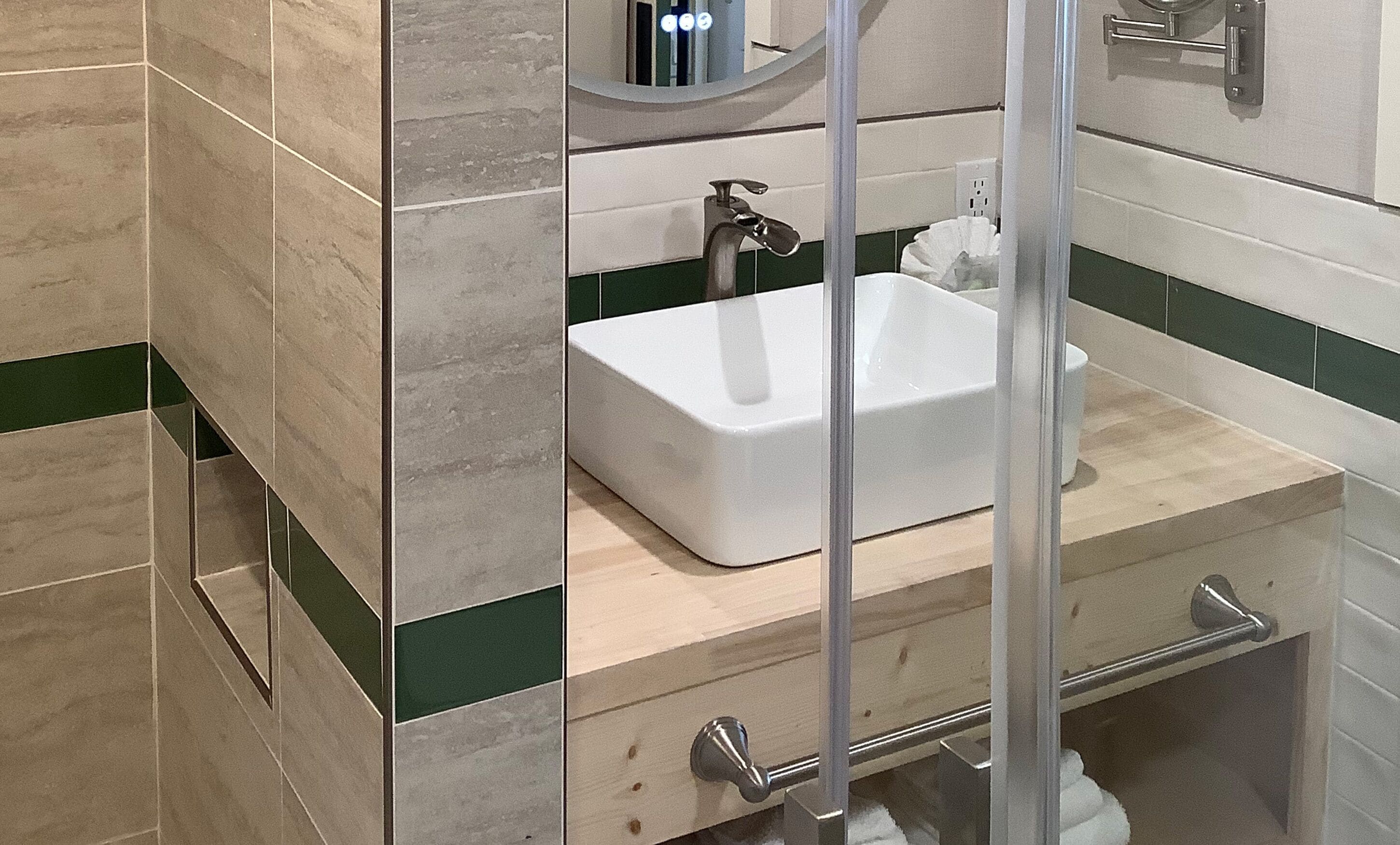 A bathroom with a white sink, green and beige tiles, a mirror, and a towel rack.