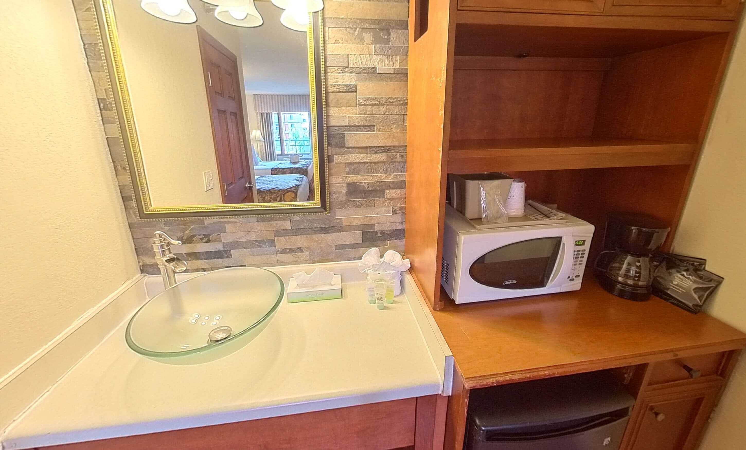A bathroom with a glass sink, a white microwave, and a wooden vanity.