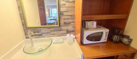 A bathroom with a glass sink, a white microwave, and a wooden vanity.