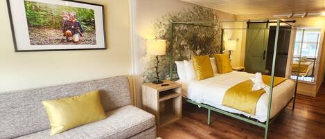 A hotel room with a bed, a sofa, a nightstand, a lamp, and a picture on the wall.