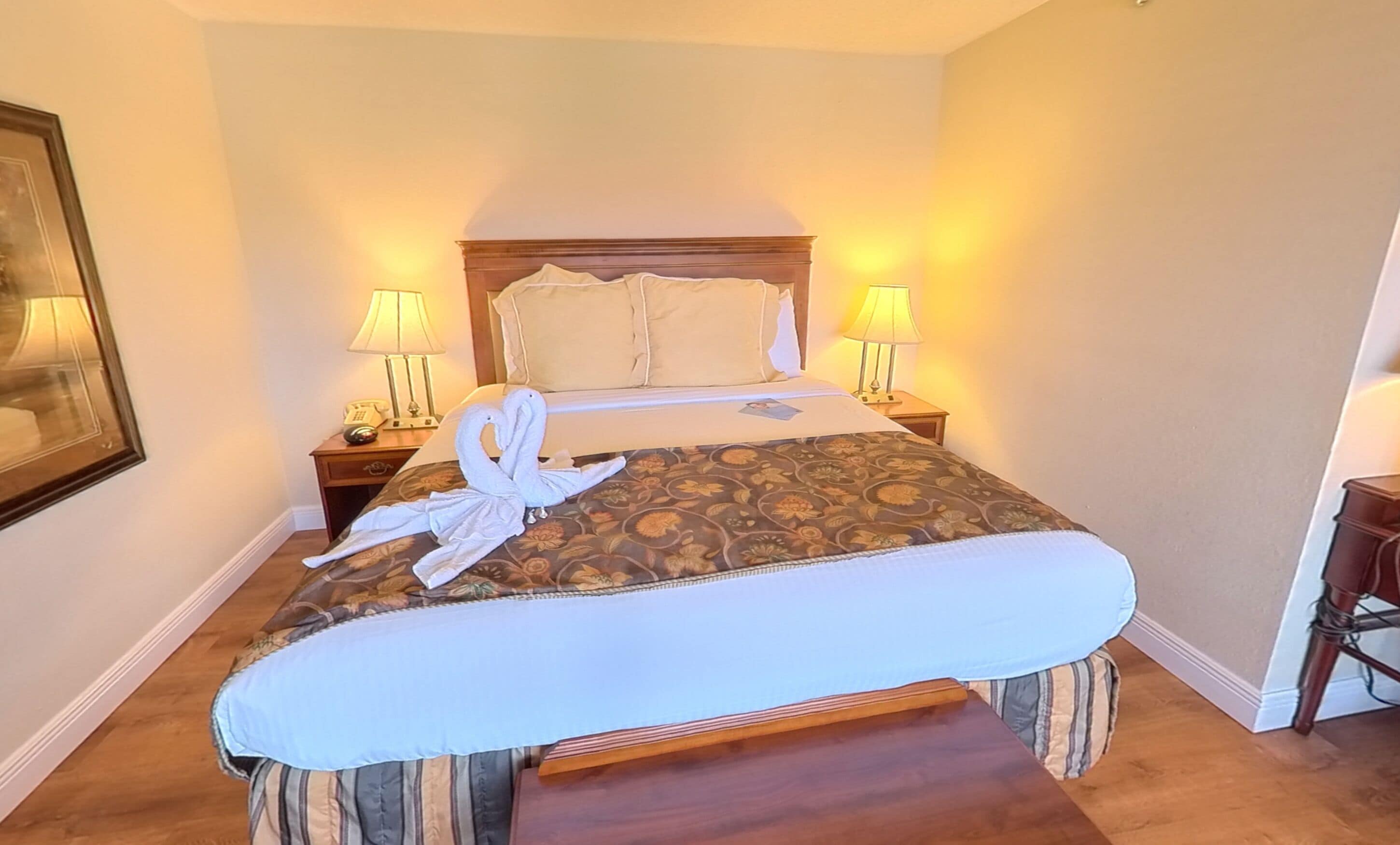 A hotel room with a bed, two bedside lamps, a telephone, and a framed picture on the wall.