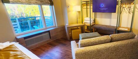 Une chambre d’hôtel comprenant un lit, un canapé, un bureau avec une lampe, une télévision et une fenêtre donnant sur des arbres.