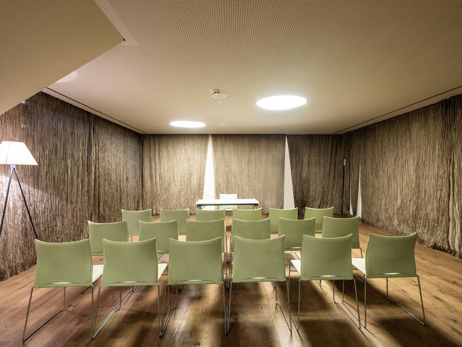 A conference room with a wooden floor, green chairs, a table, and a ceiling with recessed lighting.