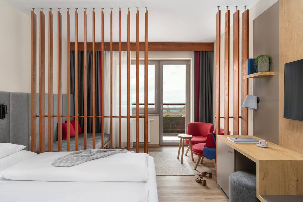 Habitación de hotel con cama, escritorio, silla, mesita y vistas al exterior.