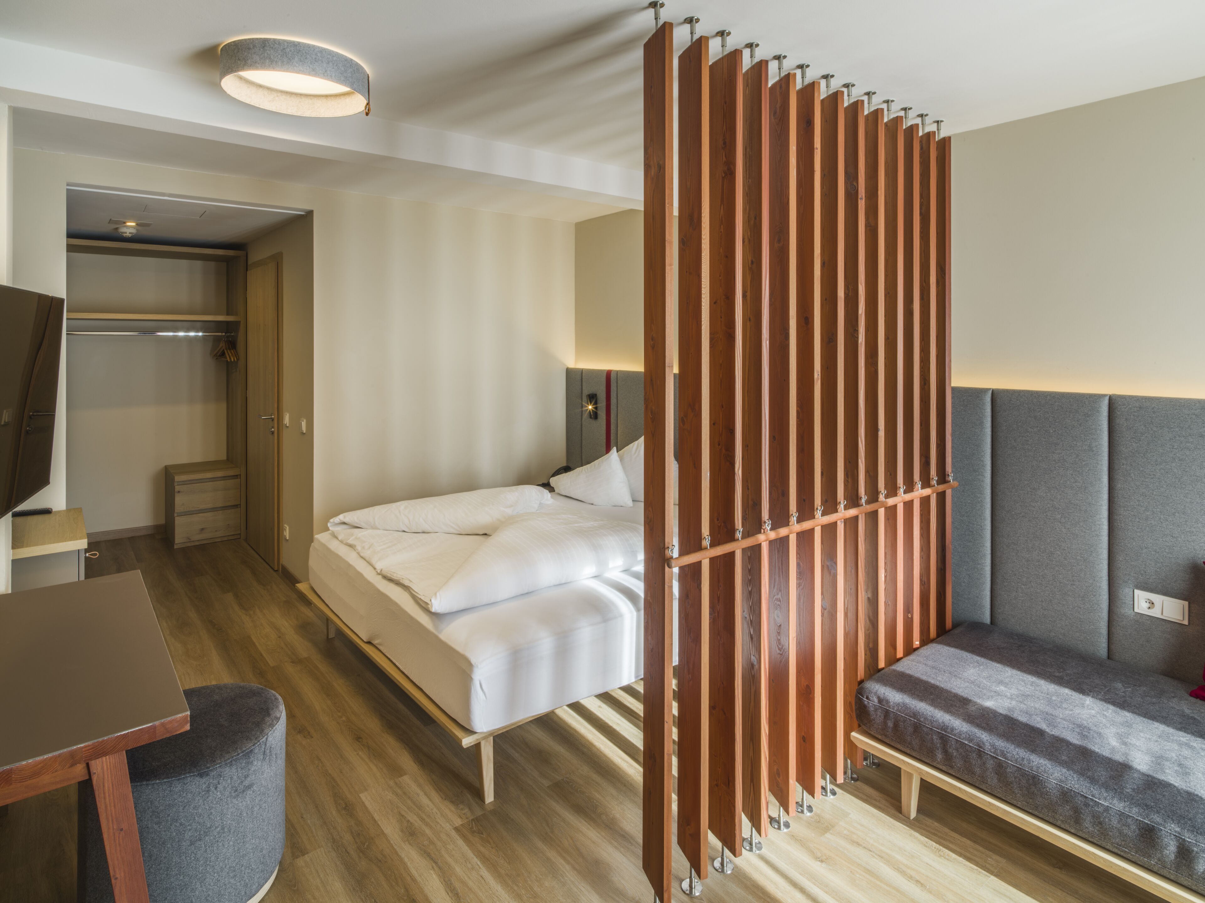 Una habitación de hotel con cama, escritorio, silla, armario y un tabique.