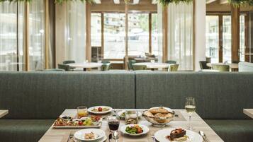 A restaurant dining area with a long table set for a meal, surrounded by green upholstered seating.