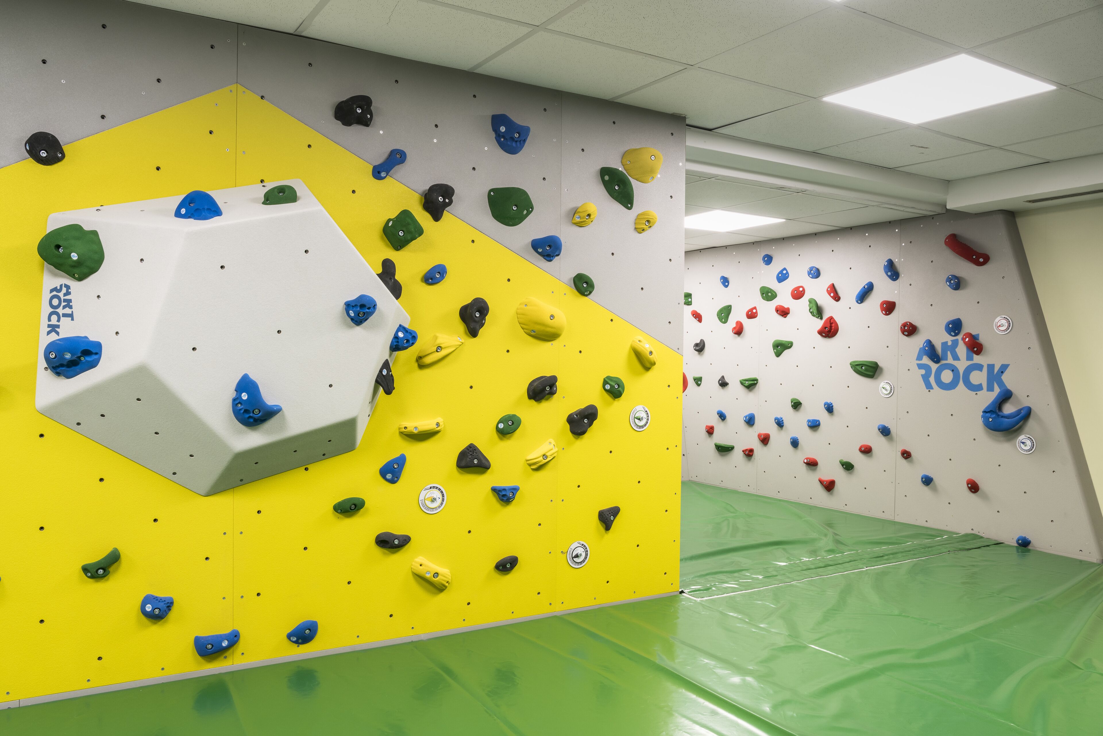 Une salle d’escalade dotée de prises de différentes couleurs et d’un grand mur d’escalade blanc.
