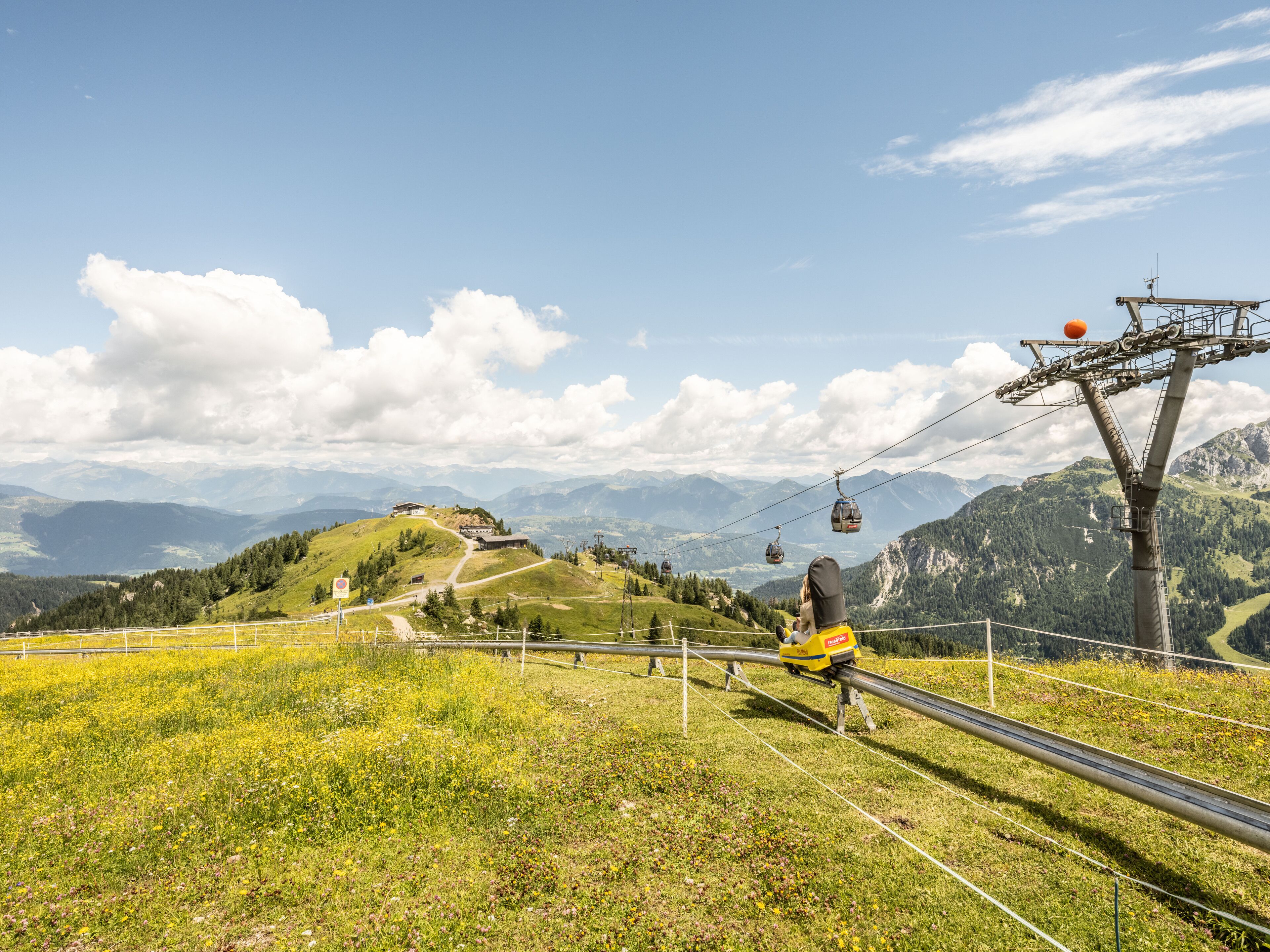 A cable car system with a person in a yellow jacket on the cable, overlooking a mountainous landscape with green hills and a clear sky.