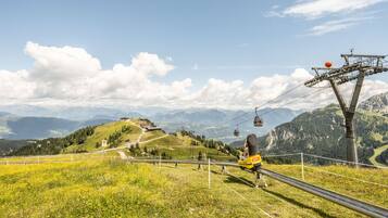 A cable car system with a person in a yellow jacket on the cable, overlooking a mountainous landscape with green hills and a clear sky.