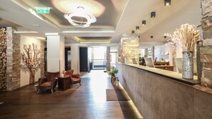 Ein Hotel-Empfangsbereich mit Steinwand, Holzboden, Ledersesseln und einer modernen Leuchte.