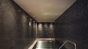 Ein moderner Wellnessbereich mit einem gläsernen Whirlpool, Metallgeländern und gefliesten Wänden.