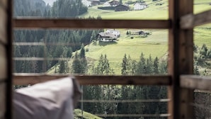 Une pièce dotée d’une grande fenêtre donnant sur une vallée verdoyante, avec des bâtiments et des arbres.