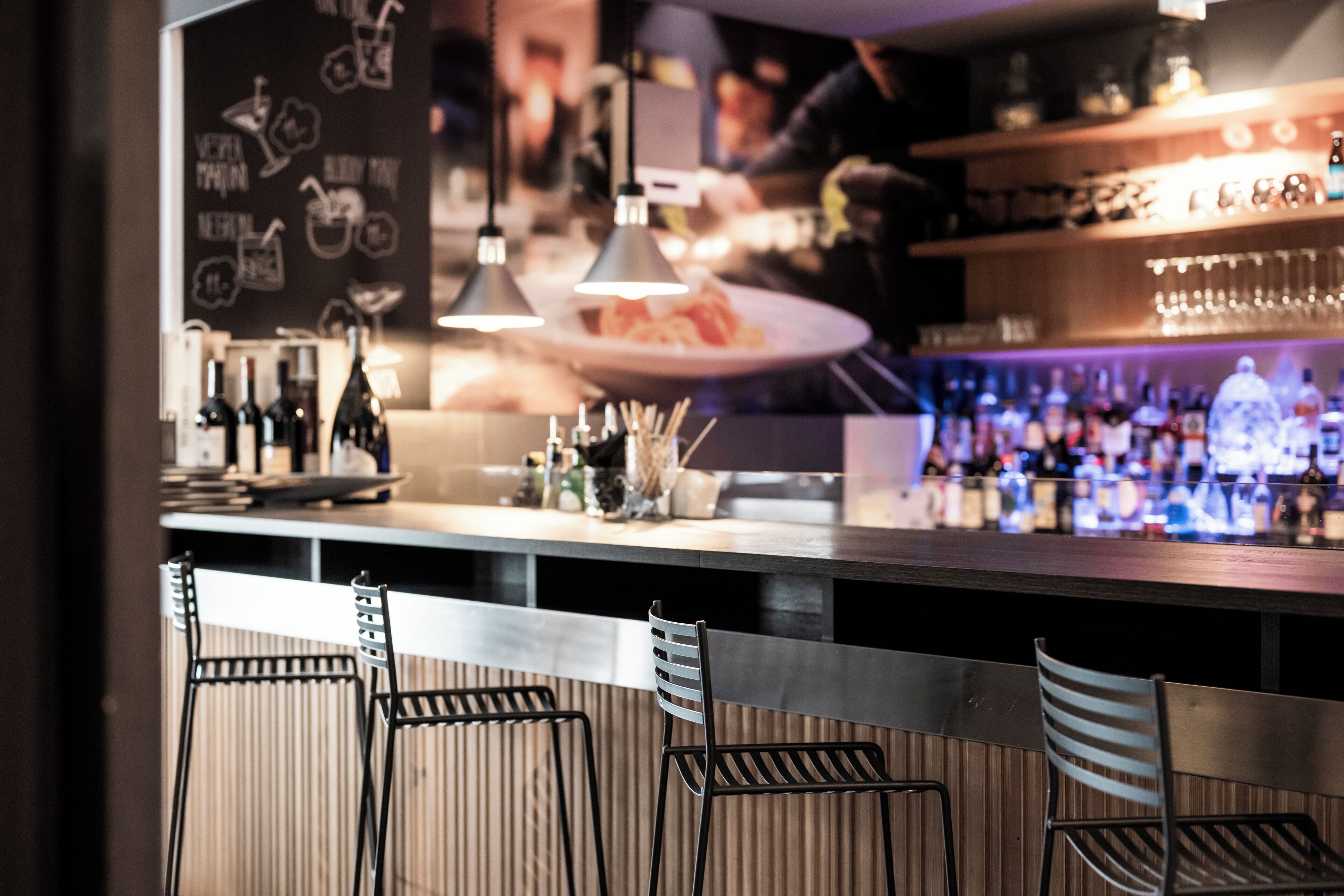 Una zona de bar con mostrador, luces colgantes y taburetes.