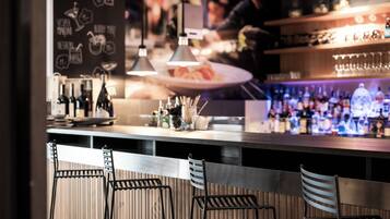 Una zona de bar con mostrador, luces colgantes y taburetes.