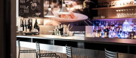 A bar area with a counter, hanging lights, and bar stools.