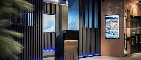 A modern lobby with vertical wooden panels, a central black reception desk, and digital displays on the walls.