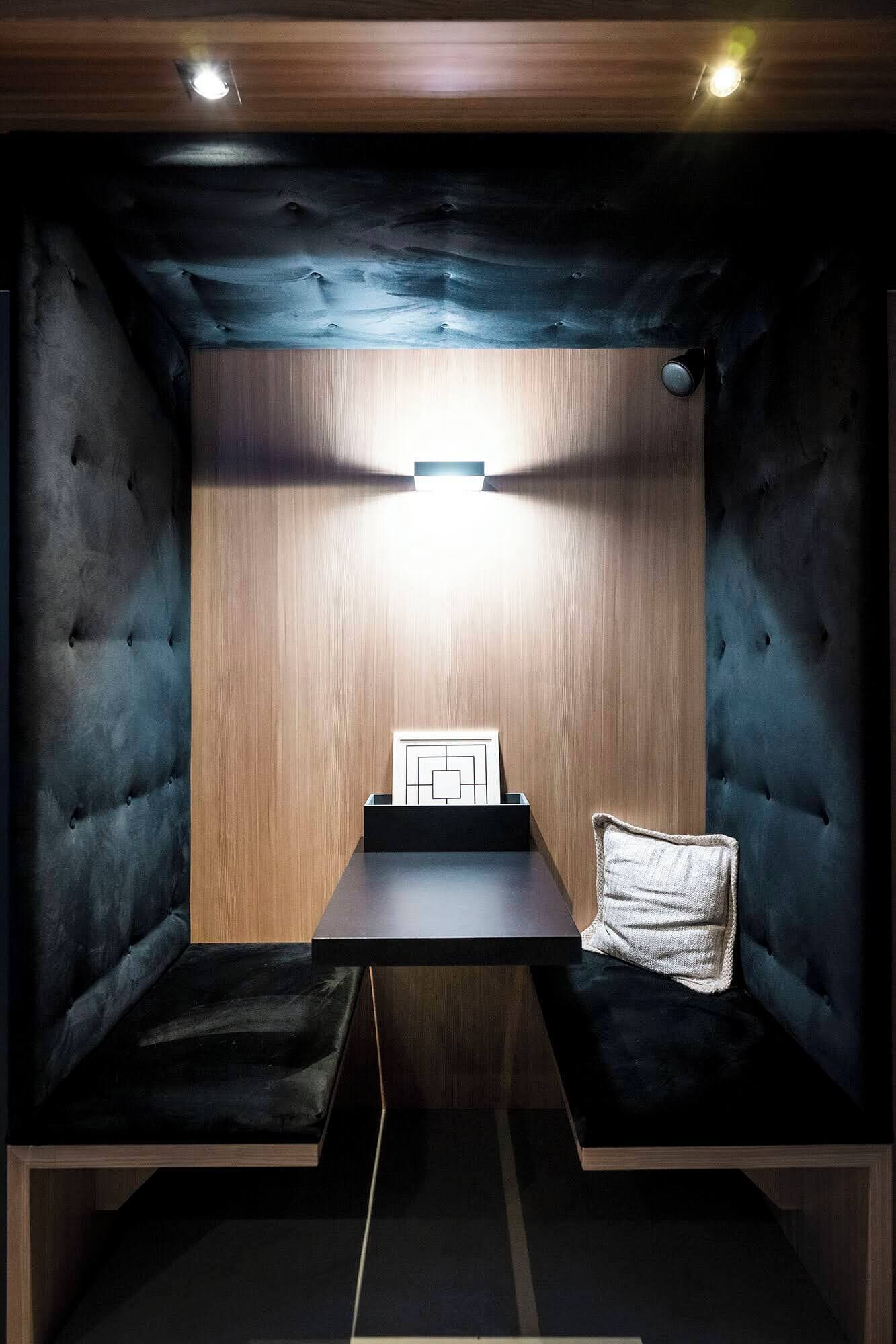 A cozy, dimly lit room with a wooden wall, a cushioned bench, and a small table with a pillow.