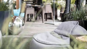 Un espace extérieur aménagé avec une table et des chaises, entouré de plantes en pot et surmonté d’un grand parasol.