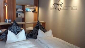 Een hotelkamer met een bed, kussens, een garderobe en een muur met de tekst 'enjoy'.
