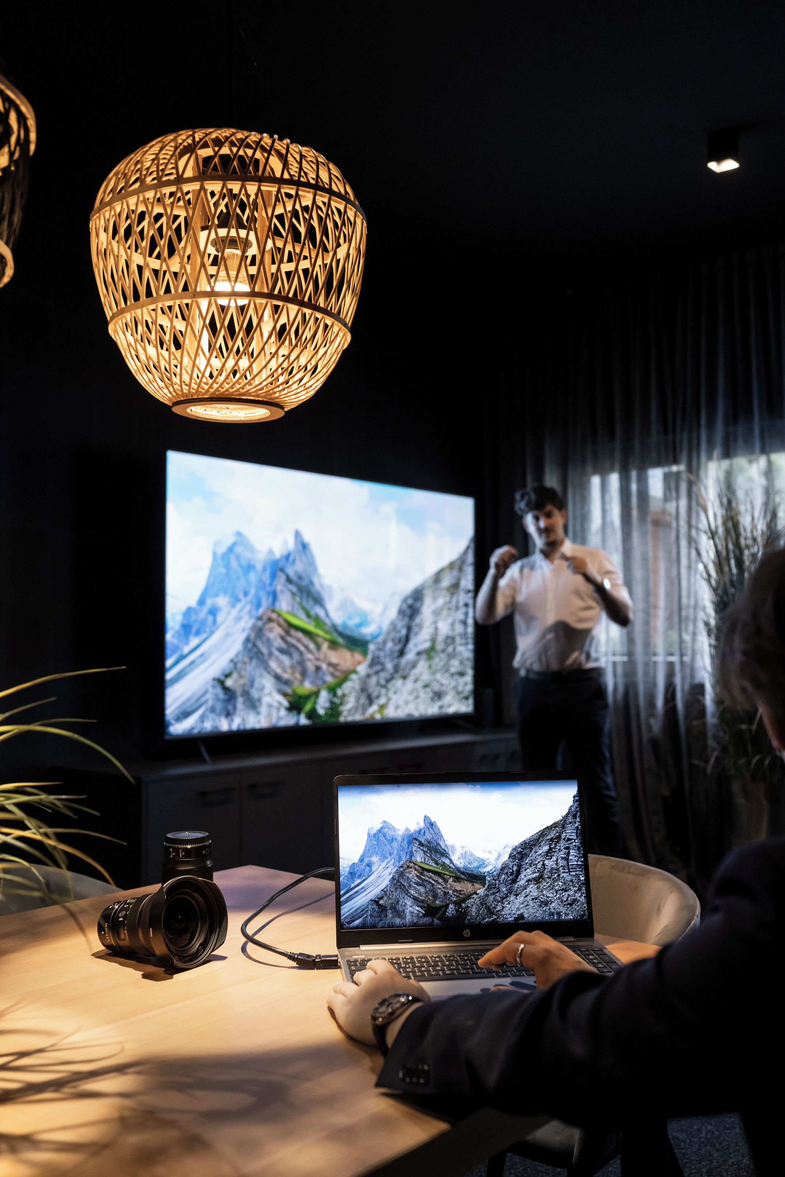 A room with a large screen displaying a mountain landscape, a laptop, and a camera on a table.