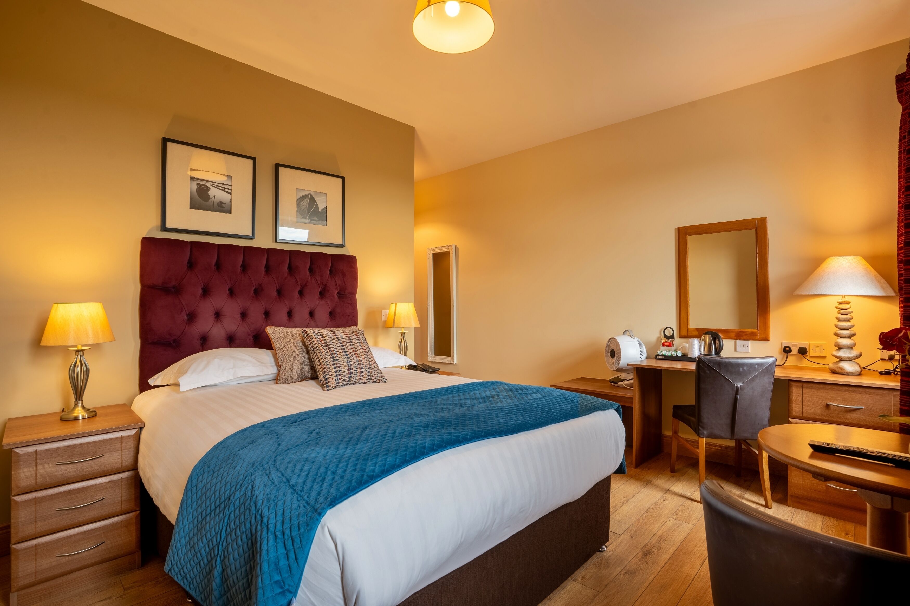 A hotel room with a large bed, a desk with a chair, a mirror, and two bedside lamps.
