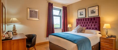 A hotel room with a bed, a desk, a chair, a bedside table, and a window with curtains.