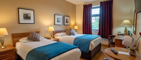 A hotel room with two beds, a desk, a chair, a lamp, and a window with curtains.