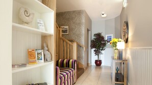 A hallway with a striped sofa, a potted plant, and a wooden staircase. - Kinvara Guesthouse (Kinvara)