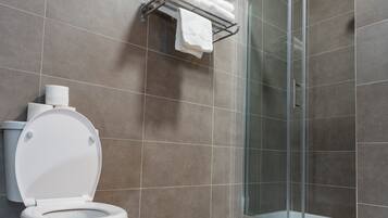 Un baño moderno con inodoro, cabina de ducha de vidrio y toallero con toallas.