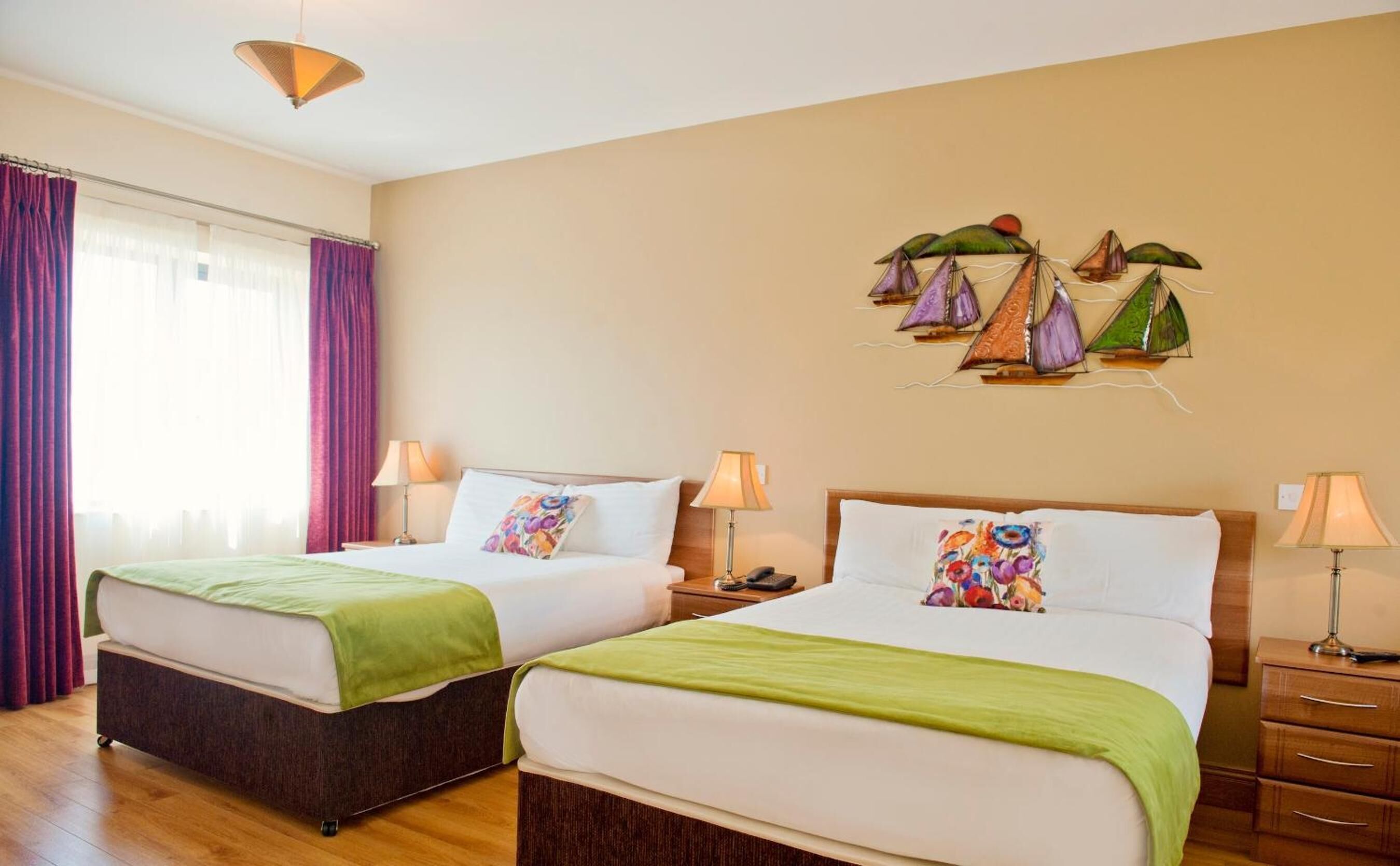 A hotel room with two beds, a large window with curtains, a wall-mounted artwork of sailboats, and a wooden floor.
