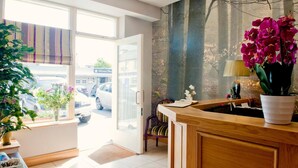 A hotel reception area with a wooden counter, a chair, and a vase of flowers. - Kinvara Guesthouse (Kinvara)