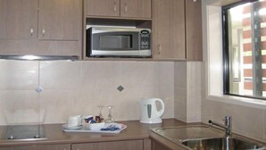 Une cuisine avec des meubles de rangement en bois, un four à micro-ondes, une bouilloire et un évier.