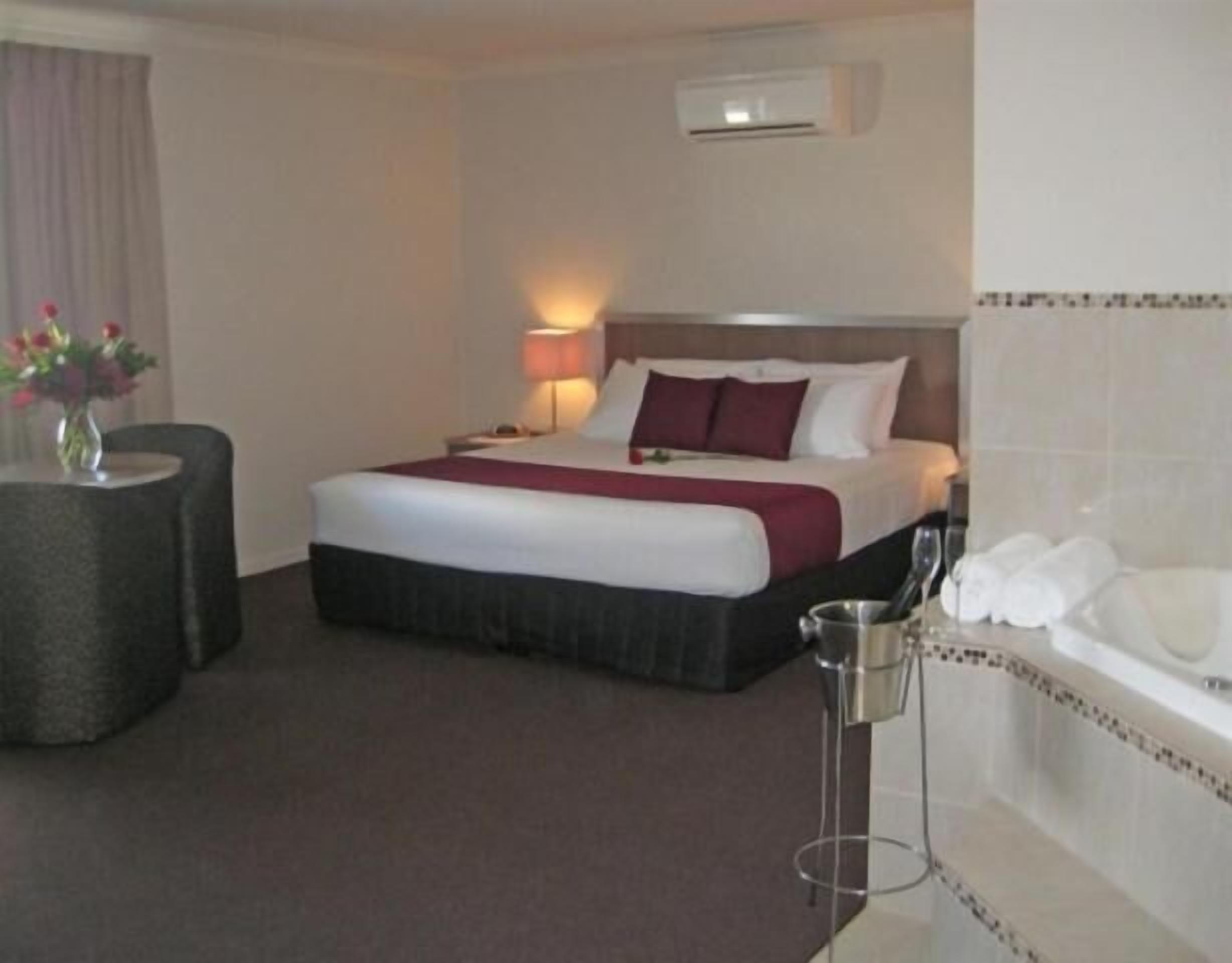 Ein Hotelzimmer mit Bett, Nachttisch, Lampe und einem kleinen Tisch mit Blumenvase.