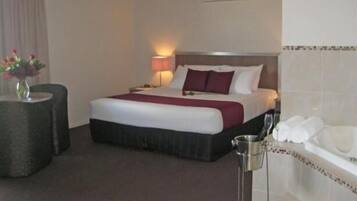 Ein Hotelzimmer mit Bett, Nachttisch, Lampe und einem kleinen Tisch mit Blumenvase.