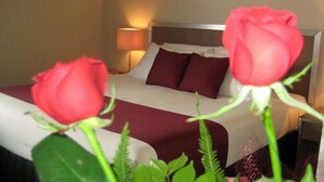 Une chambre d’hôtel avec un lit, une table de chevet et deux roses rouges au premier plan.