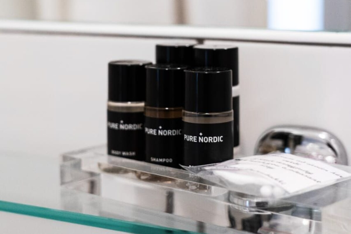 A bathroom with a glass shelf holding three black bottles labeled "PURE NORDIC" and a white container.