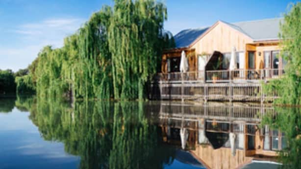 A lakeside cabin with a reflection in the water, a wooden deck, and a large window overlooking the lake. - Perricoota Vines Retreat (Moama)