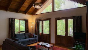A spacious living room with a high ceiling, large windows, a sofa, a coffee table, and a television. - Perricoota Vines Retreat (Moama)