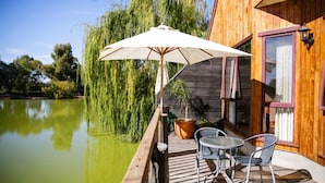 A wooden deck with a table and chairs, overlooking a calm body of water and a weeping willow tree. - Perricoota Vines Retreat (Moama)