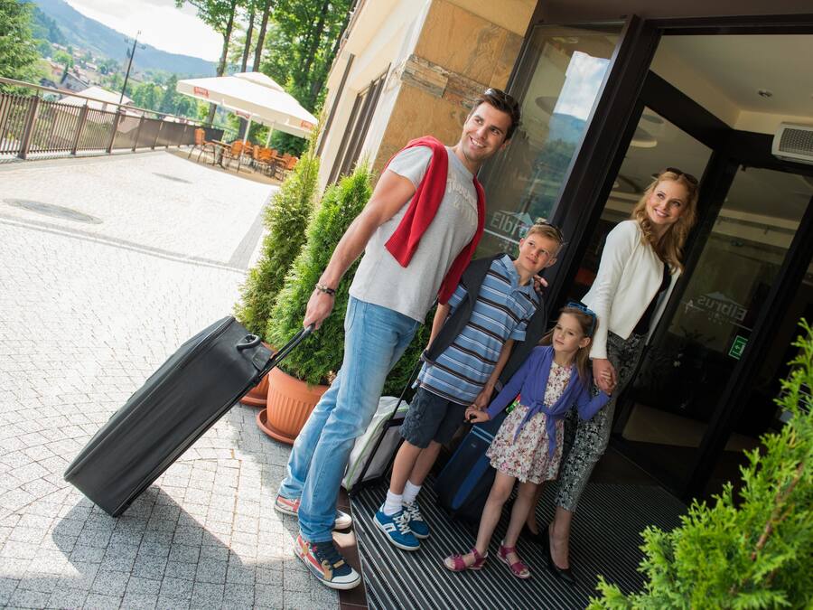 Eine Familie mit einem Mann, der einen Koffer hält, steht vor einem Gebäude mit Glastür.