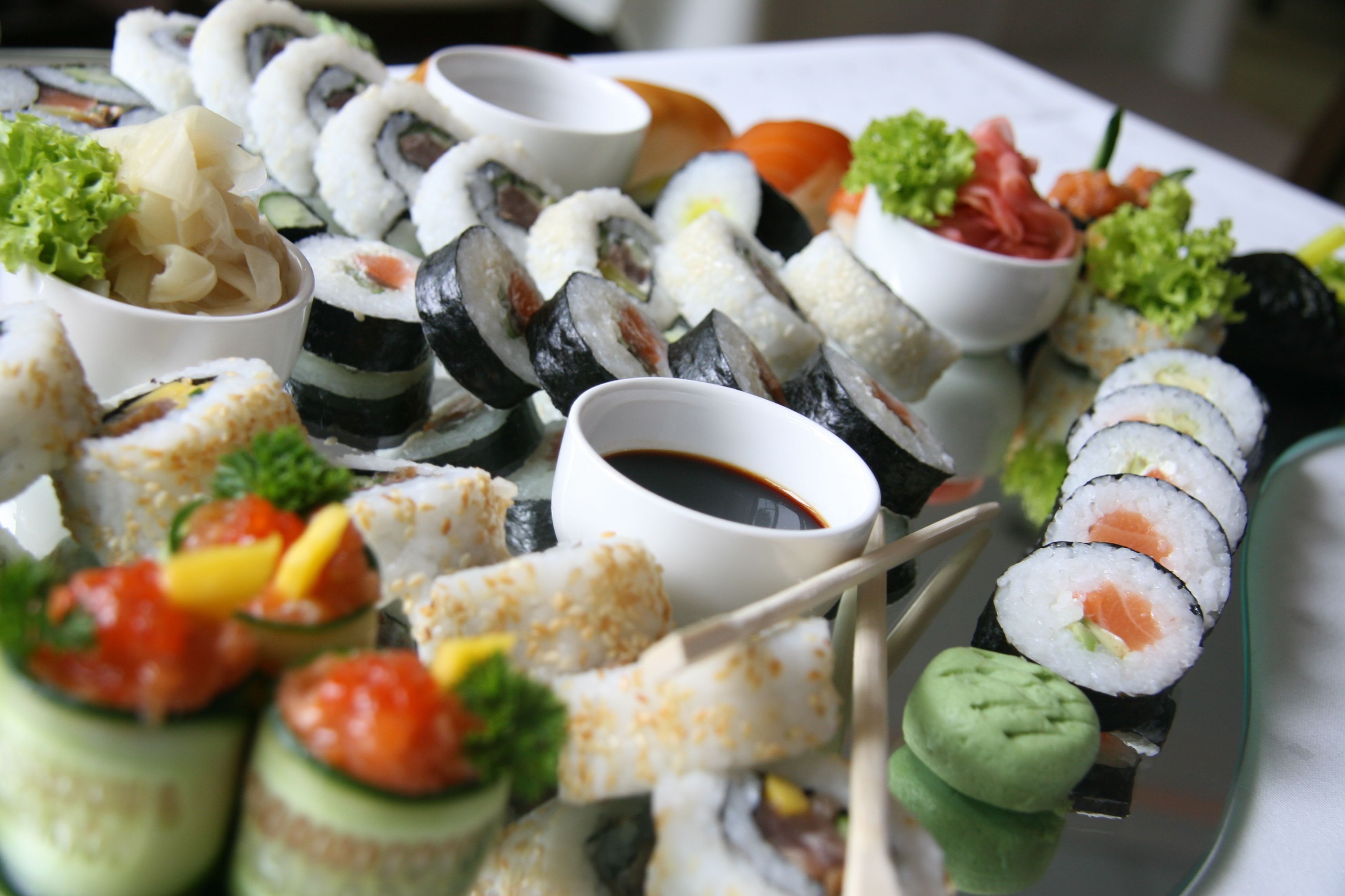Diversos tipos de sushi e nigiri em um prato de vidro, acompanhados de pequenas tigelas de molho de soja e wasabi.