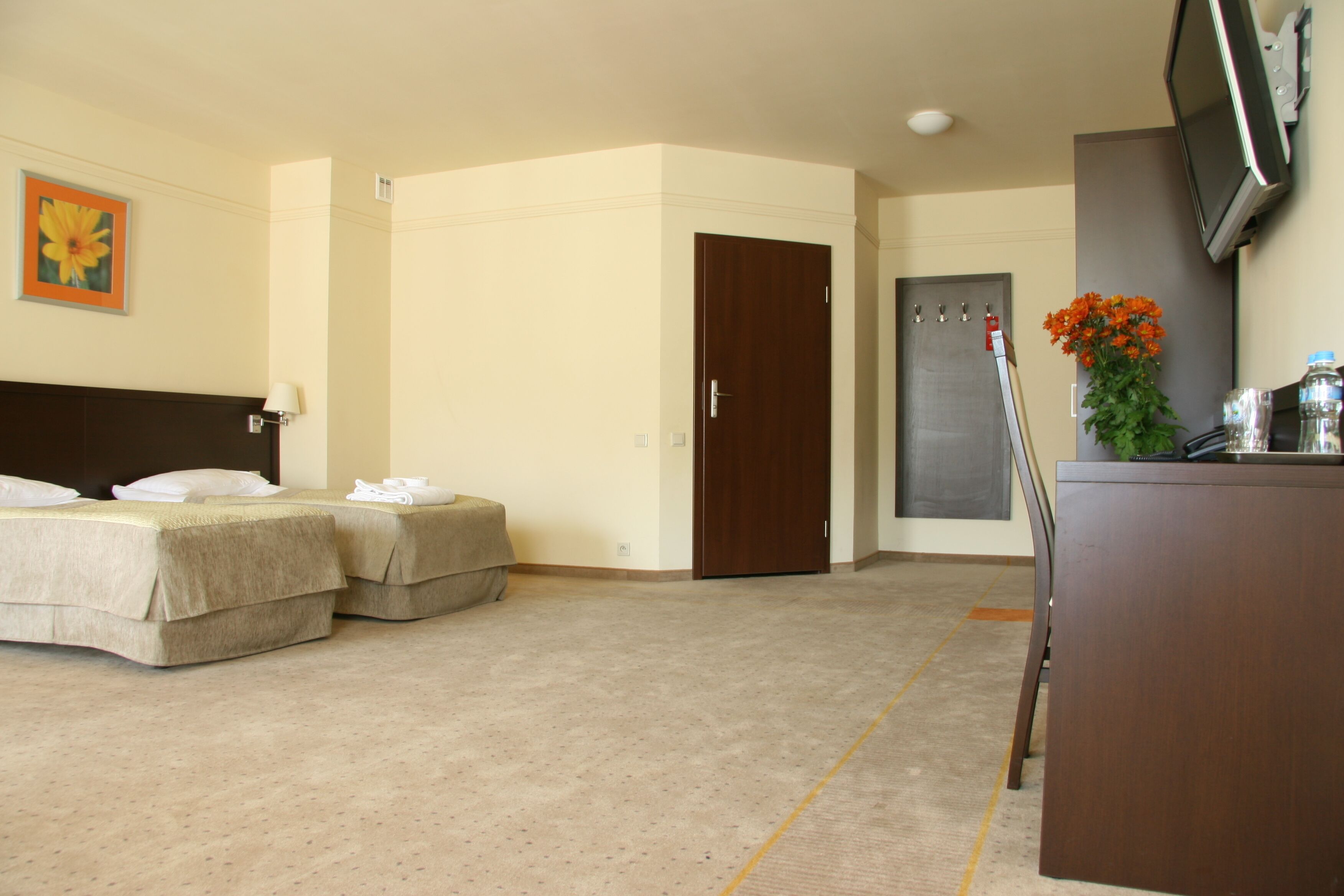A hotel room with two beds, a desk, a TV, and a door.