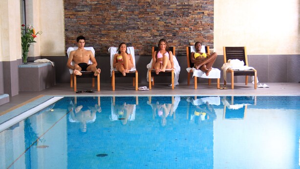 Un área junto a la piscina con sillones de descanso y un muro de piedra.