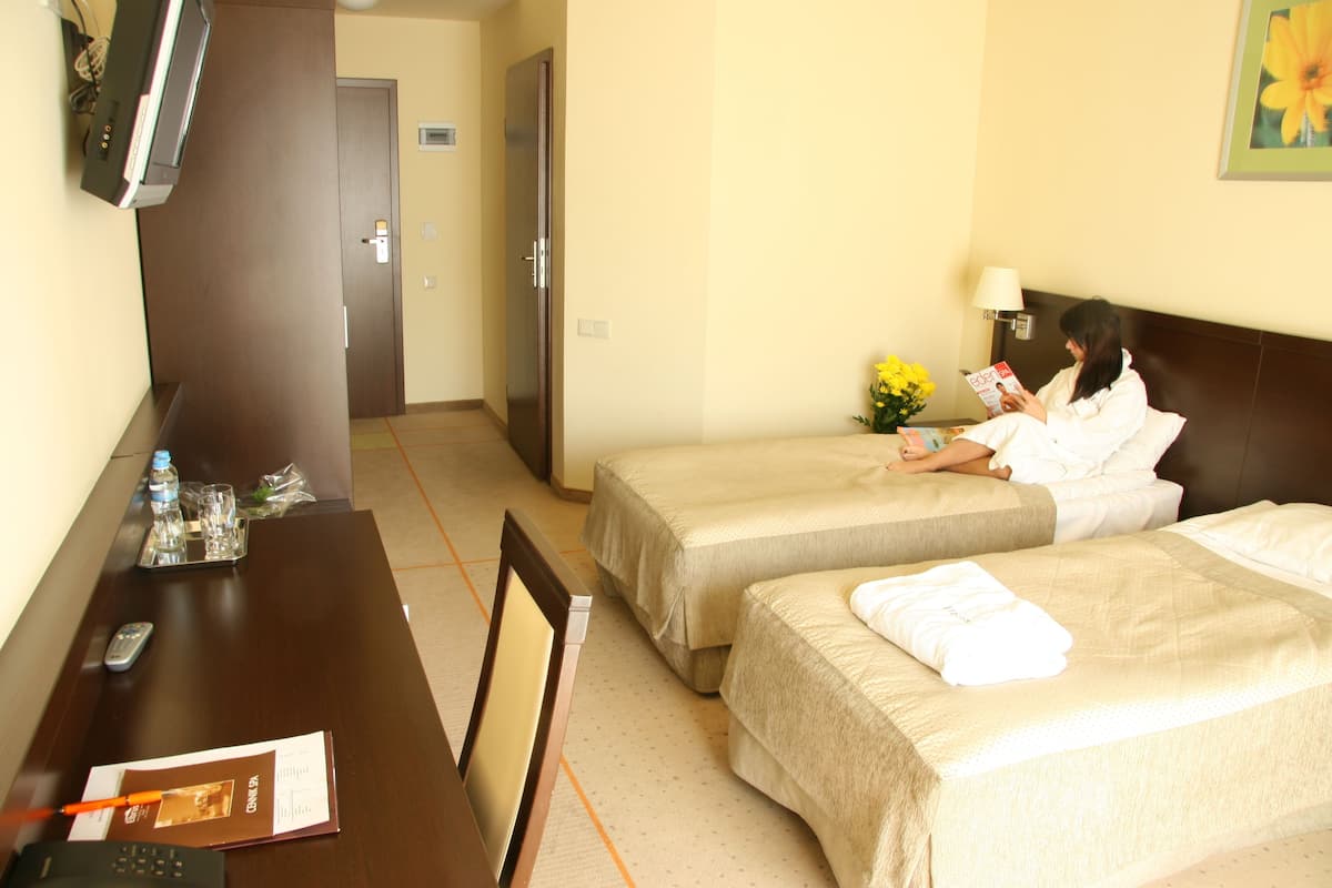 Habitación de hotel con dos camas, un escritorio con un control remoto, una revista y un jarrón con flores.