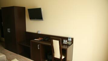 Habitación de hotel con escritorio, silla, televisor y armario.