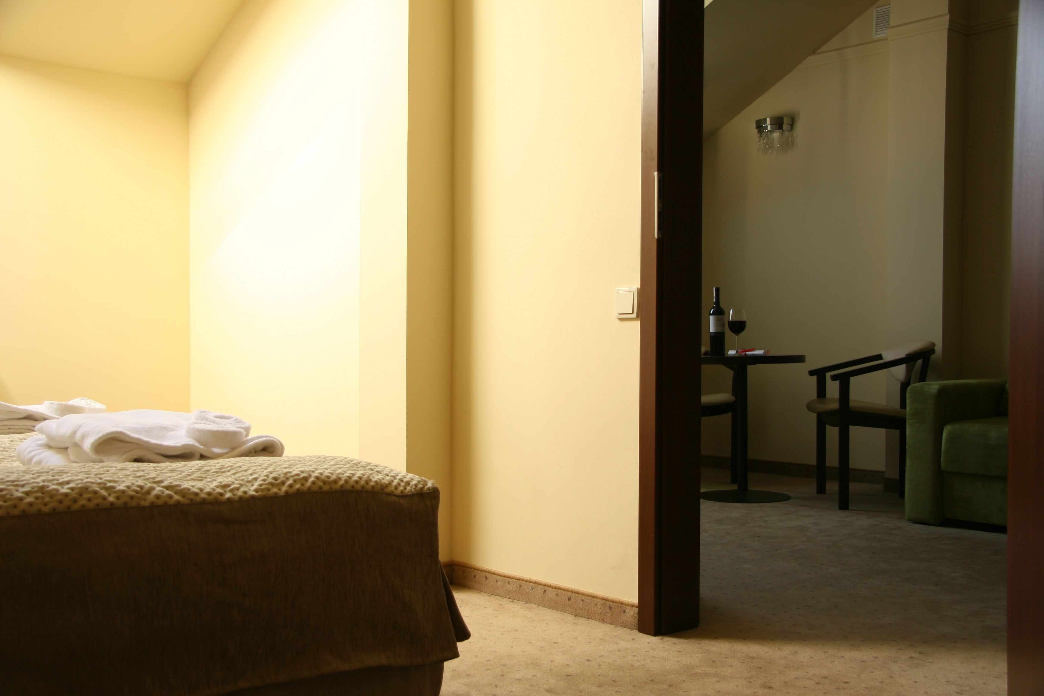 A hotel room with a bed, a chair, a small table with a bottle and glass, and a shower area.