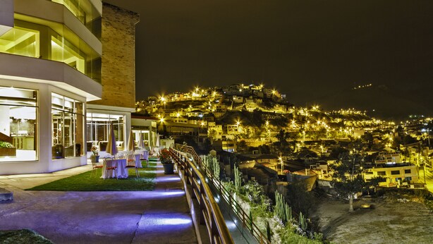 A hotel with a terrace, outdoor seating, and a view of a hillside town at night. - Hotel Ambato (Ambato)