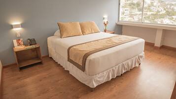 A neatly arranged bedroom with a large bed, two bedside tables, and a window offering a view of the city.