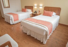 Habitación de hotel con dos camas, piso de madera y una mesita de noche con teléfono y lámpara.