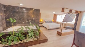 A modern hotel room with a marble wall, a bed, a TV, and a plant. - Hotel Ambato (Ambato)